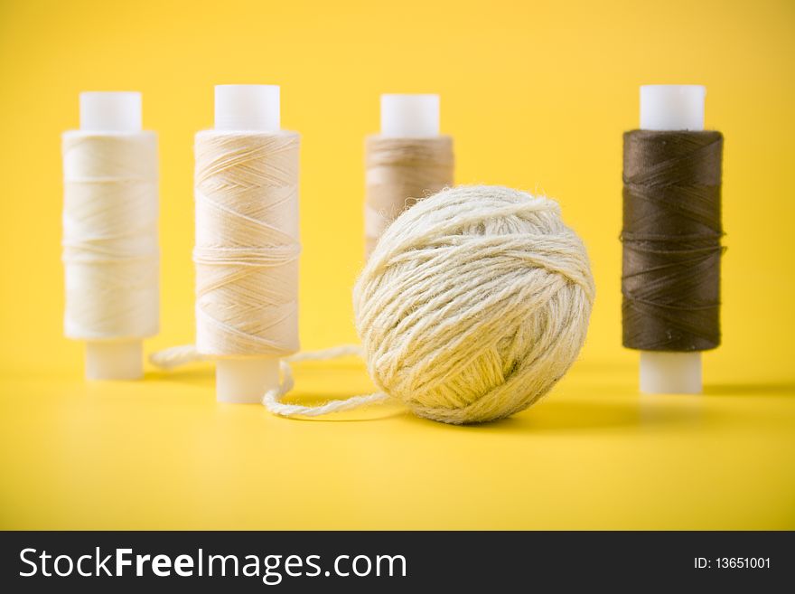 Ball of yarn and spools of thread on a yellow background