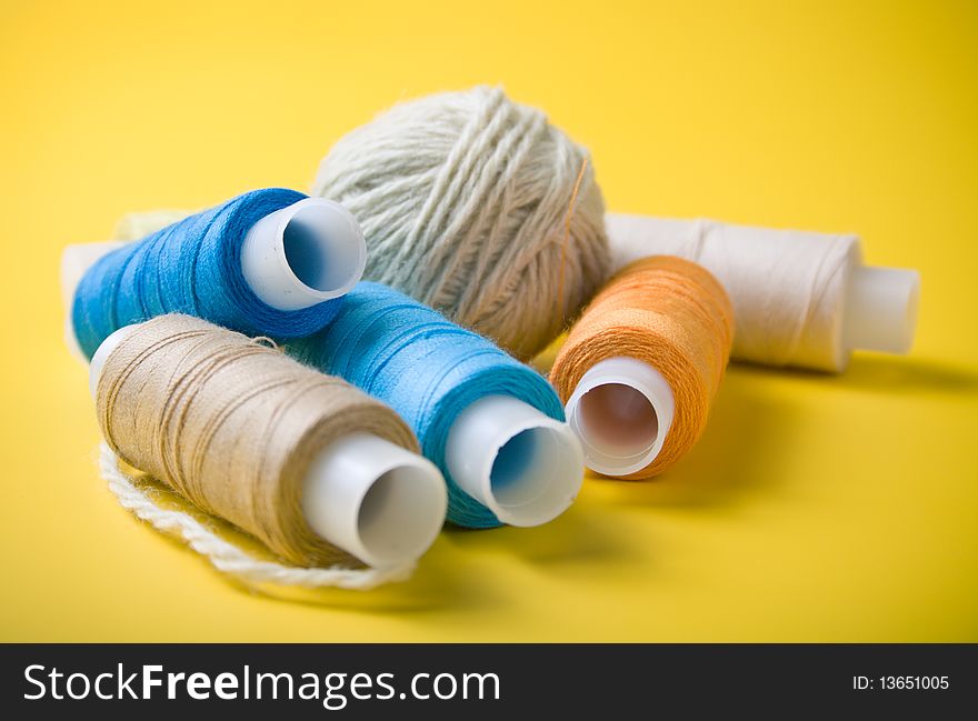 Ball of yarn and spools of thread on a yellow background
