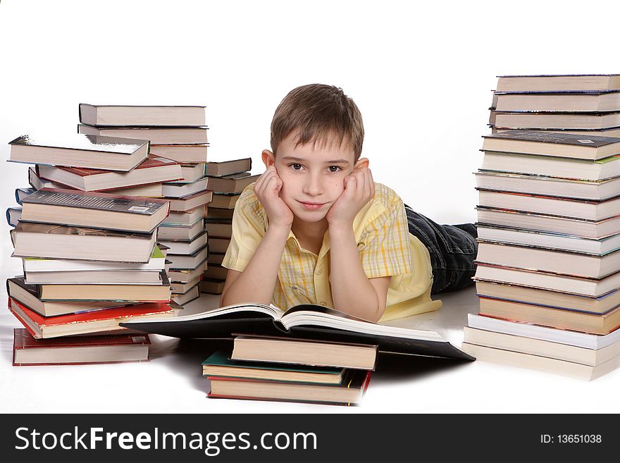 Young boy lies between a piles of books reading against a white background. Young boy lies between a piles of books reading against a white background
