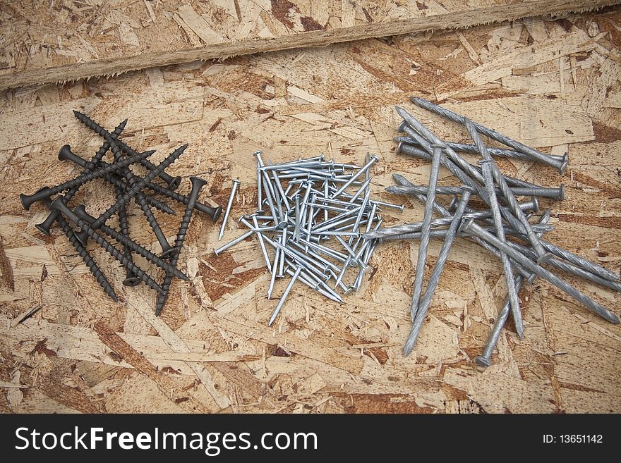 A pile of nails and screws sit on some wood ready for construction. A pile of nails and screws sit on some wood ready for construction