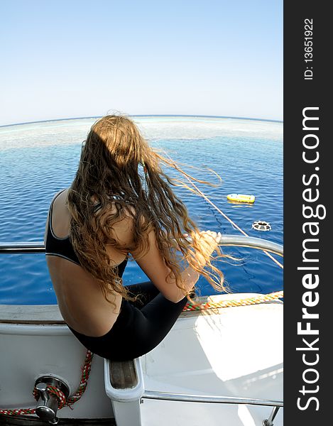 Young girl with long hair looking at the sea, while sitting on board the yacht. view from the back. Young girl with long hair looking at the sea, while sitting on board the yacht. view from the back.