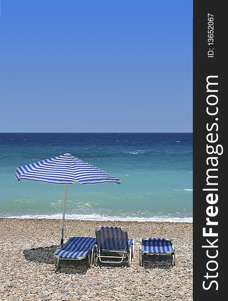 Three sunbeds on pebble beach by turquoise blue sea. Three sunbeds on pebble beach by turquoise blue sea