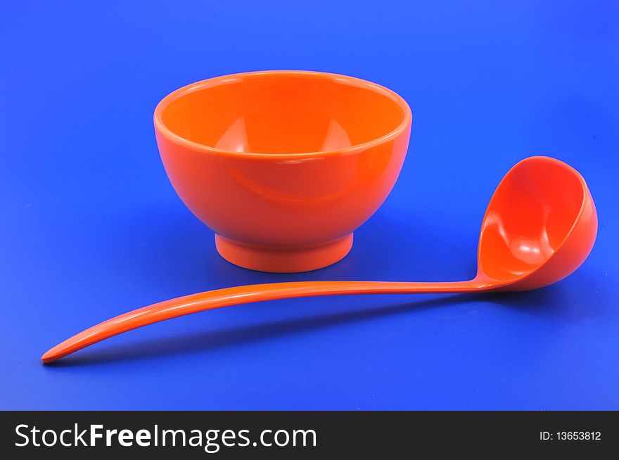 Bowl and ladle made of plastic red photographed in front of blue background