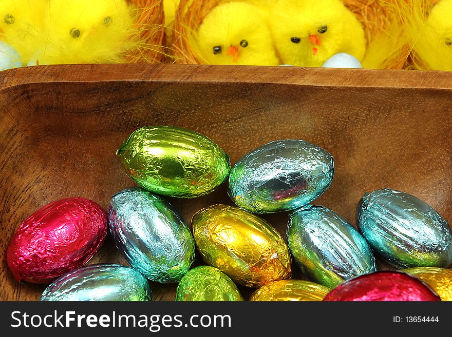 Colorful Chocolate Easter eggs in wooden bowl and yellow chicks in background. Colorful Chocolate Easter eggs in wooden bowl and yellow chicks in background