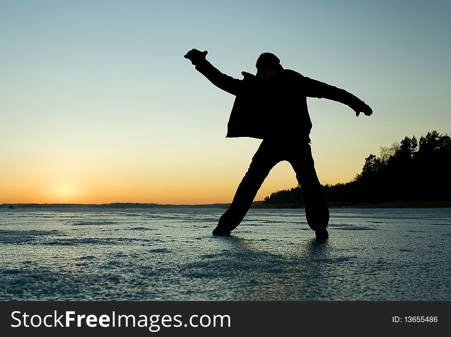 Silhouette of a man glidin on ice at sunset