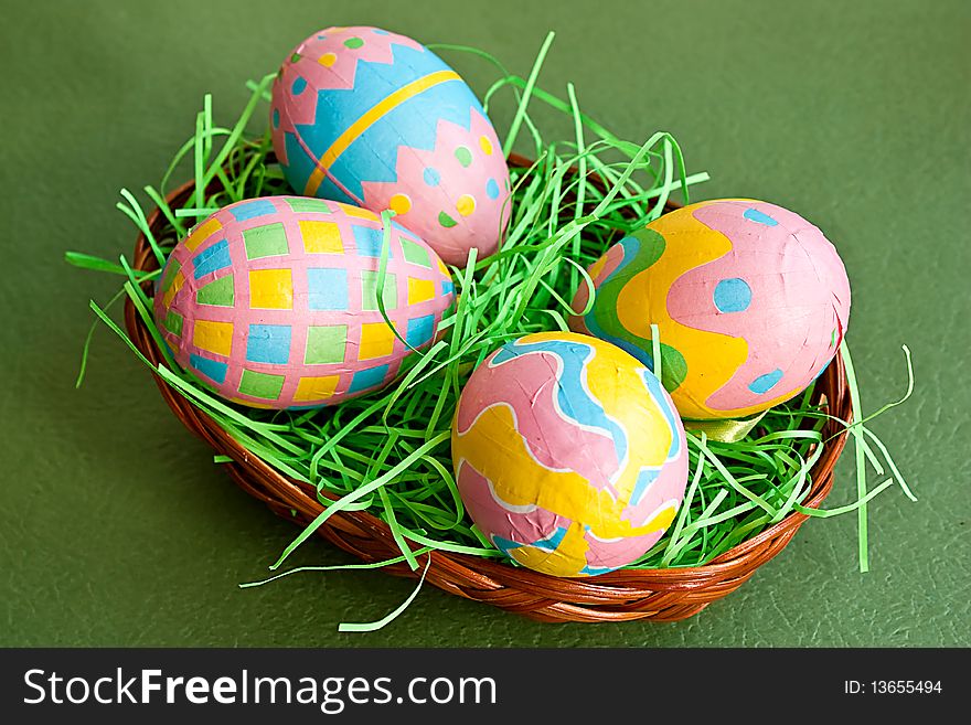 Colored Easter eggs in a basket on green background