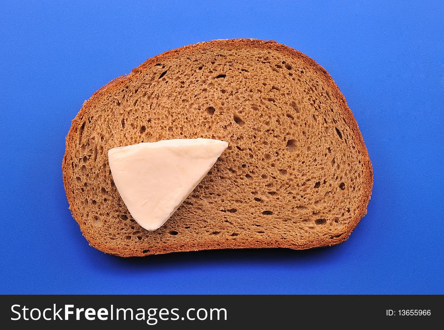 A slice of black bread, cheese and milk in front of blue background. A slice of black bread, cheese and milk in front of blue background