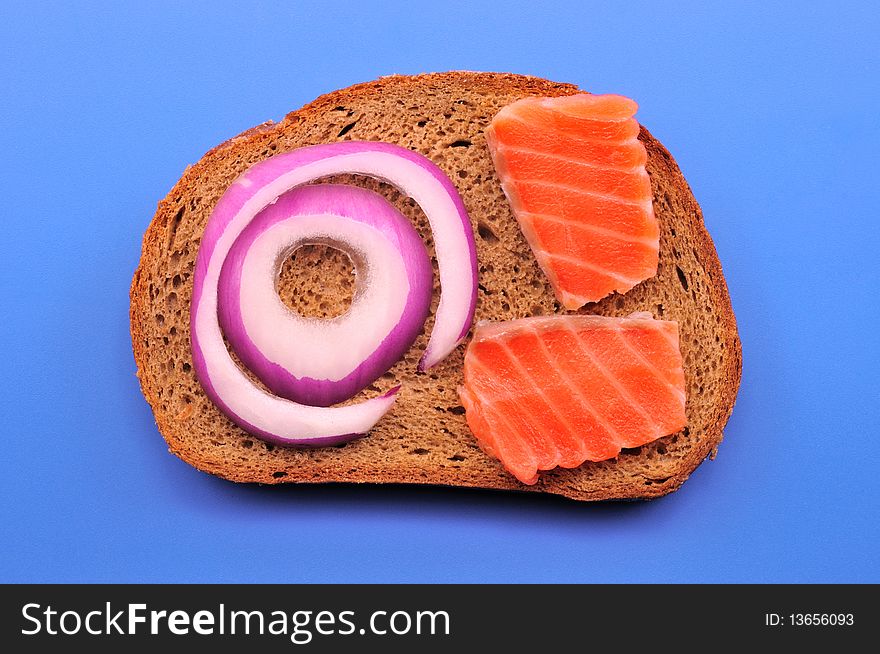 A slice of black bread and two pieces of salmon and onion rings and blue on blue. A slice of black bread and two pieces of salmon and onion rings and blue on blue