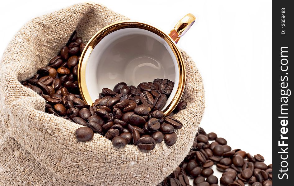 The cup lies in a sack with coffee grains is isolated on white