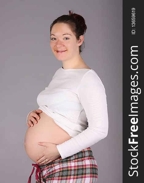 Pregnant woman holding belly on grey background