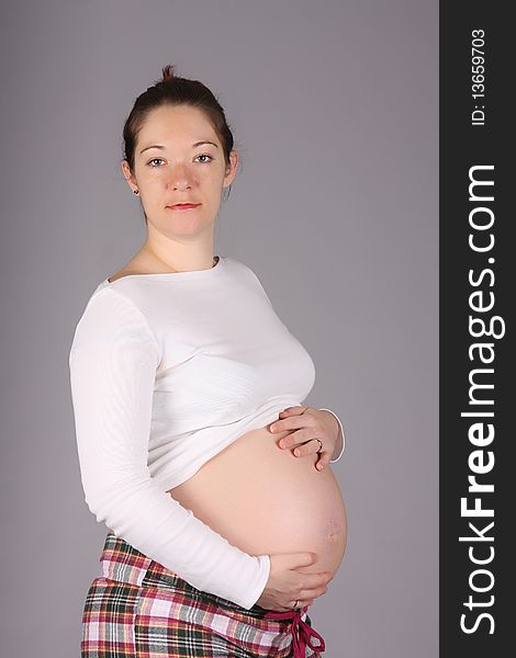Pregnant woman holding belly on grey background