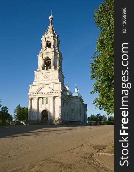 High bell tower of white church on evening light