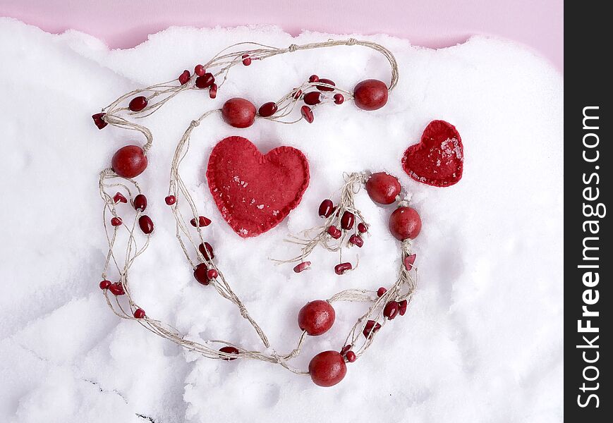 Red wooden beads, felt handmade hearts on the snow, top view, concept of congratulations on Valentine`s Day