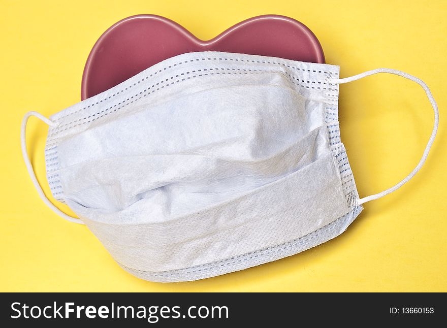 Surgical Mask over a Heart on a Yellow Background.  Good image for heart health or surgery. Surgical Mask over a Heart on a Yellow Background.  Good image for heart health or surgery.