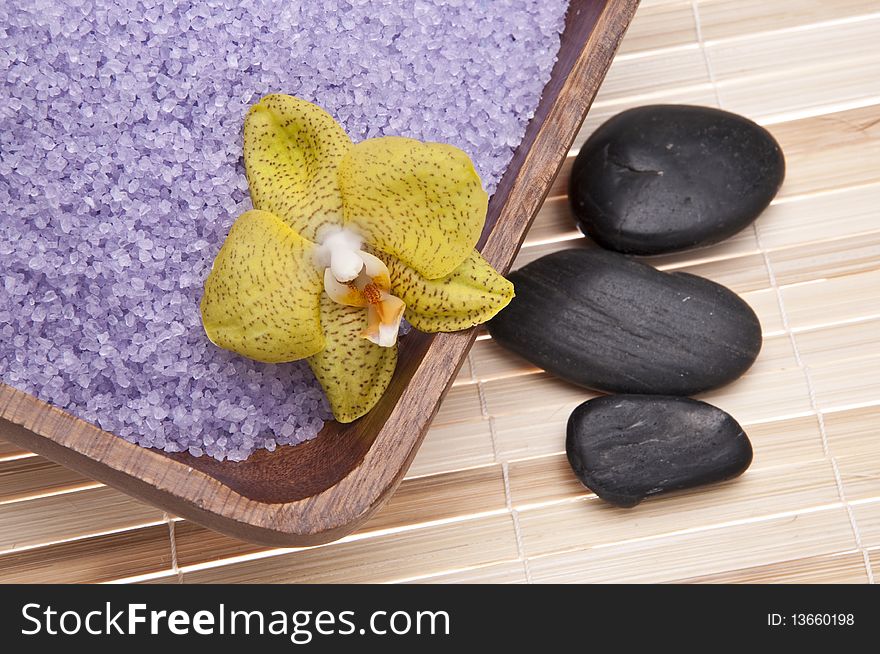 Spa scene with orchids, bath salts and massage stones on a bamboo mat.