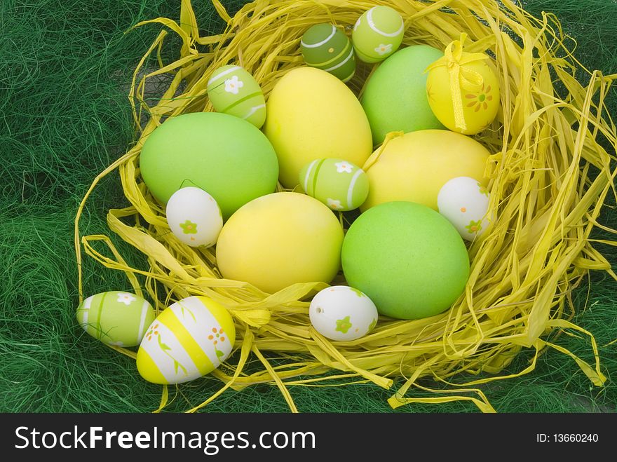 Colorful painted Easter eggs in the yellow straw nest on the green grass