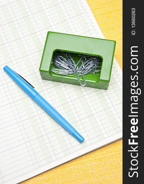 Paperclips, and a pen sit on a ruled page on a yellow background for the modern office worker. Paperclips, and a pen sit on a ruled page on a yellow background for the modern office worker.