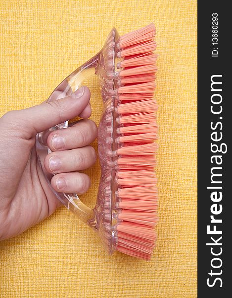 Caucasian hand holds a bright scrub brush on a yellow background in this spring cleaning themed image.