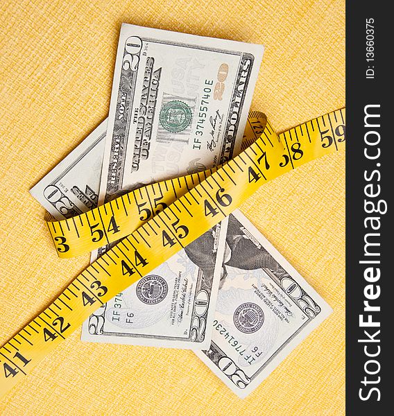 American currency is squeezed by a yellow measuring tape on a measuring background to demonstrate that money is tight.