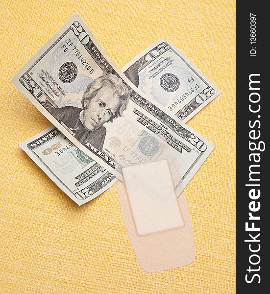 Money with a band aid on a yellow background to demonstrate the cost of health care.