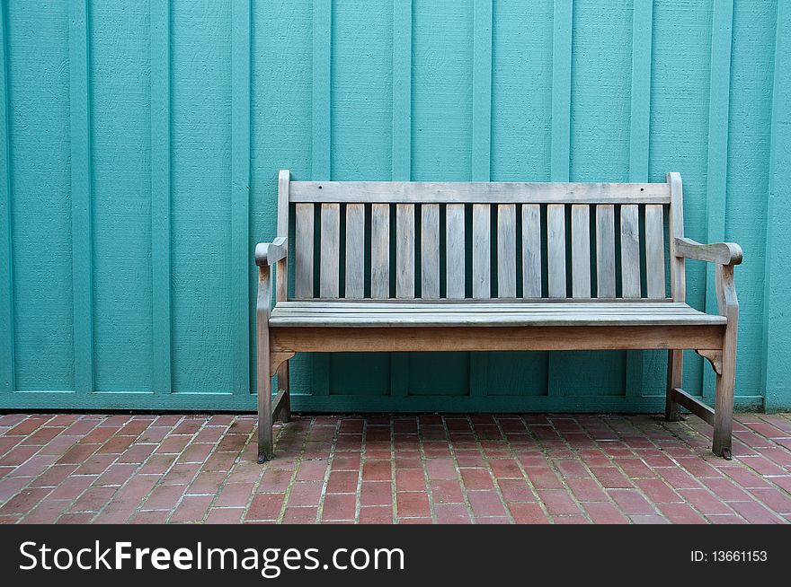 A weathered wood bench sits on bricks against blue wall