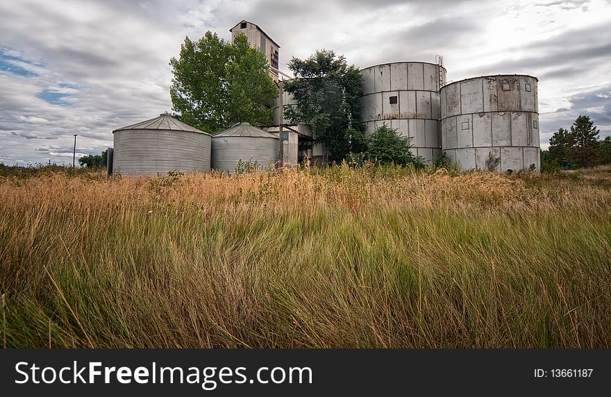 Wind blown grass with rusty silos against cloudy background. Wind blown grass with rusty silos against cloudy background