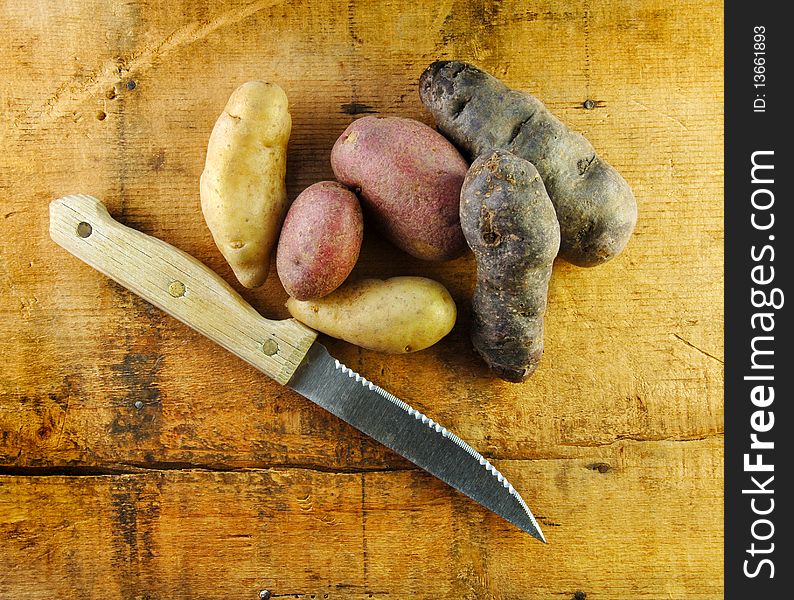 Fingerling potatoes in three colors on a rustic table with a knife. Fingerling potatoes in three colors on a rustic table with a knife.