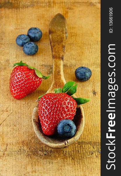 Fresh strawberries and blueberries in a wooden spoon on rustic wooden table. Fresh strawberries and blueberries in a wooden spoon on rustic wooden table.