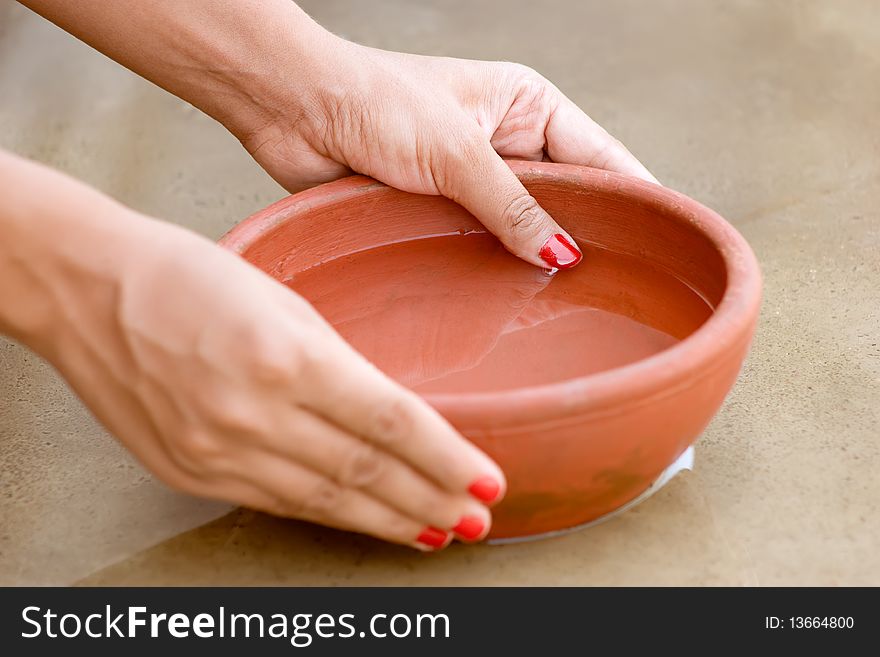 Clay red bow holding by beautiful hand  filled with water and its reflection in water on floor