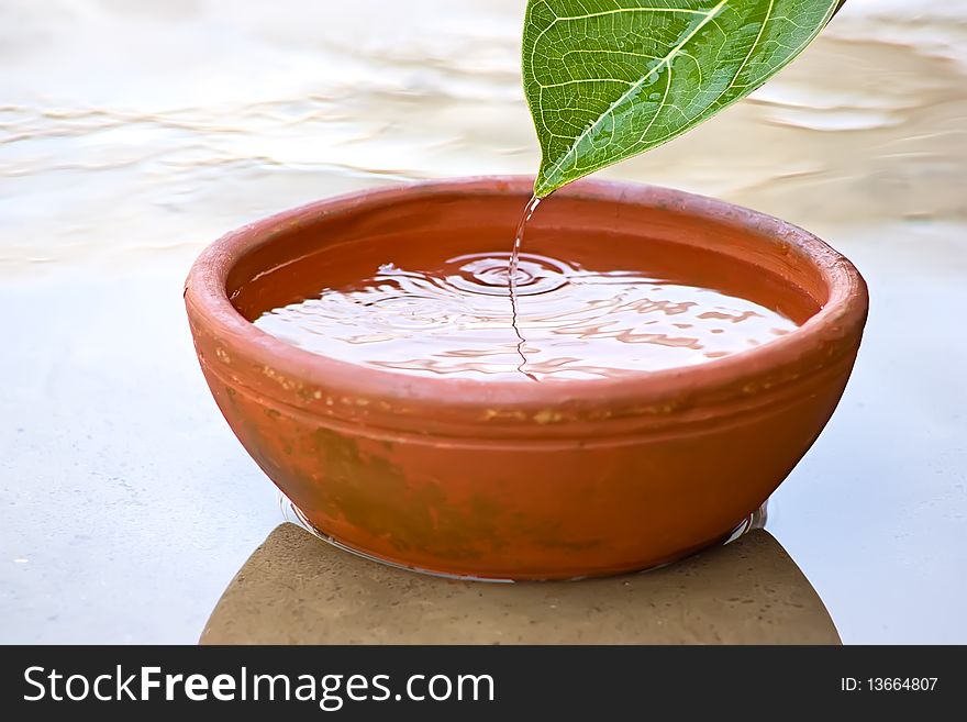 Dropping Water drops from green leaf into red clay bowl. Dropping Water drops from green leaf into red clay bowl