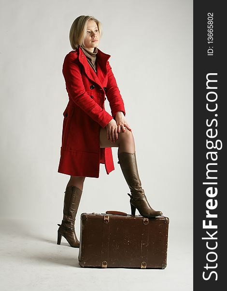 The beautiful young girl-blonde dressed in a brown dress and a red coat. The girl with a suitcase. The beautiful young girl-blonde dressed in a brown dress and a red coat. The girl with a suitcase.