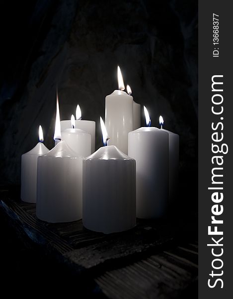 Several white candles burning on a dark background