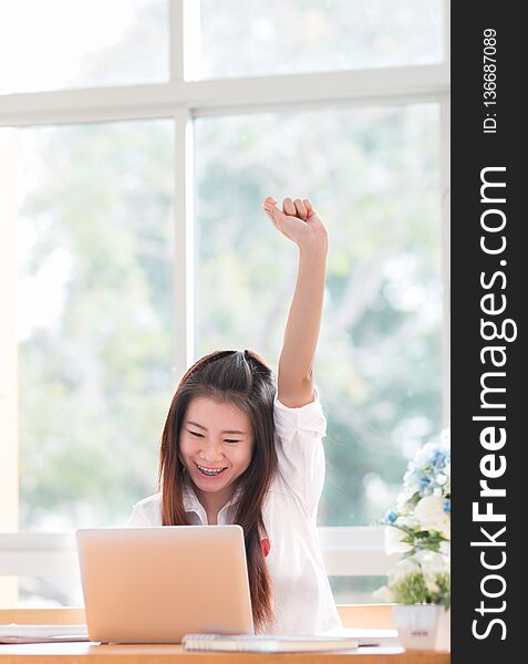 Portrait of happy Asian woman manager sitting at her laptop computer in work office, raised hands up with smiling because her
