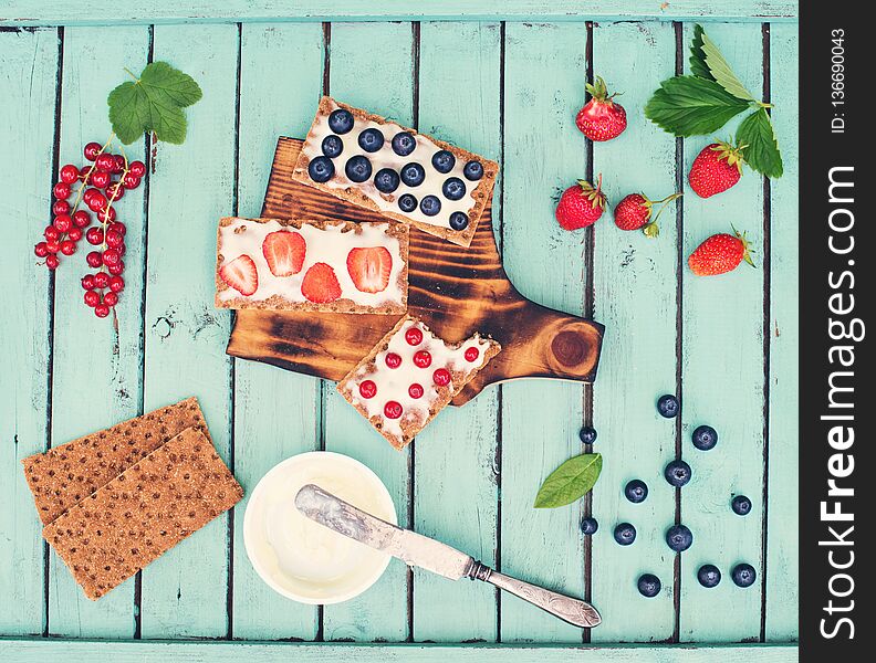 Healthy sandwiches with soft cheese and berries on bread crisps on shabby chic background. Healthy eating and summer gifts concept