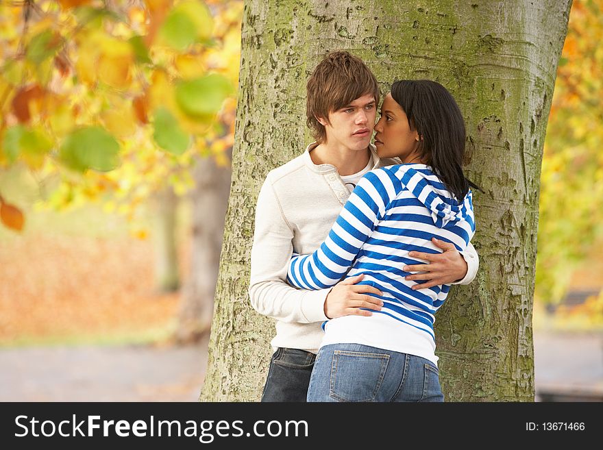 Romantic Teenage Couple By Tree In Autumn Park looking away from camera