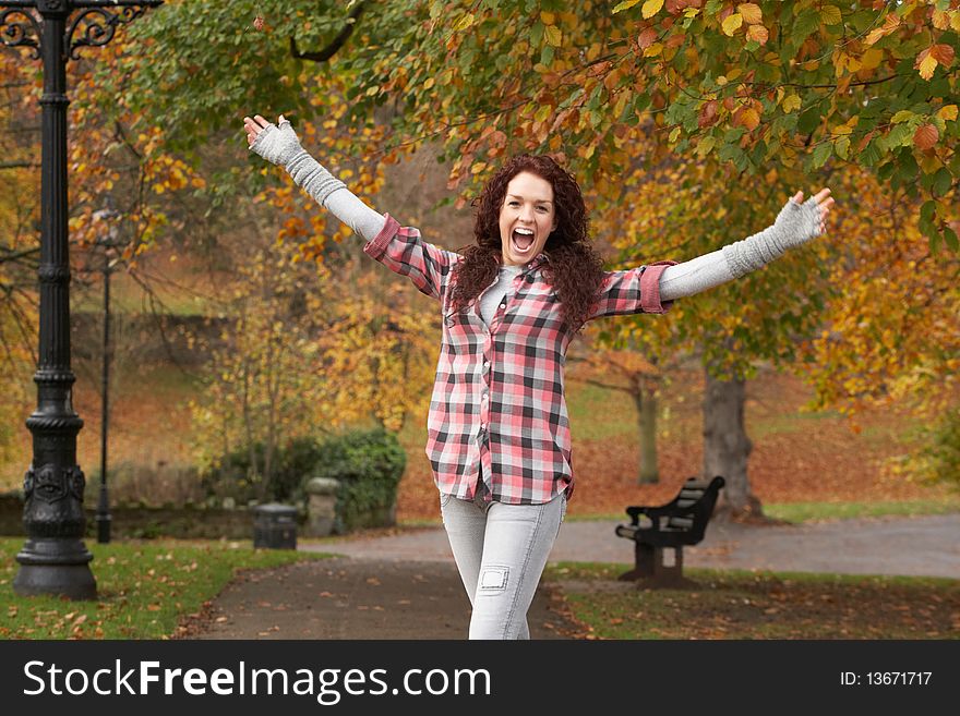 Teenage Girl Standing In Autumn Park With Arms Outstretched