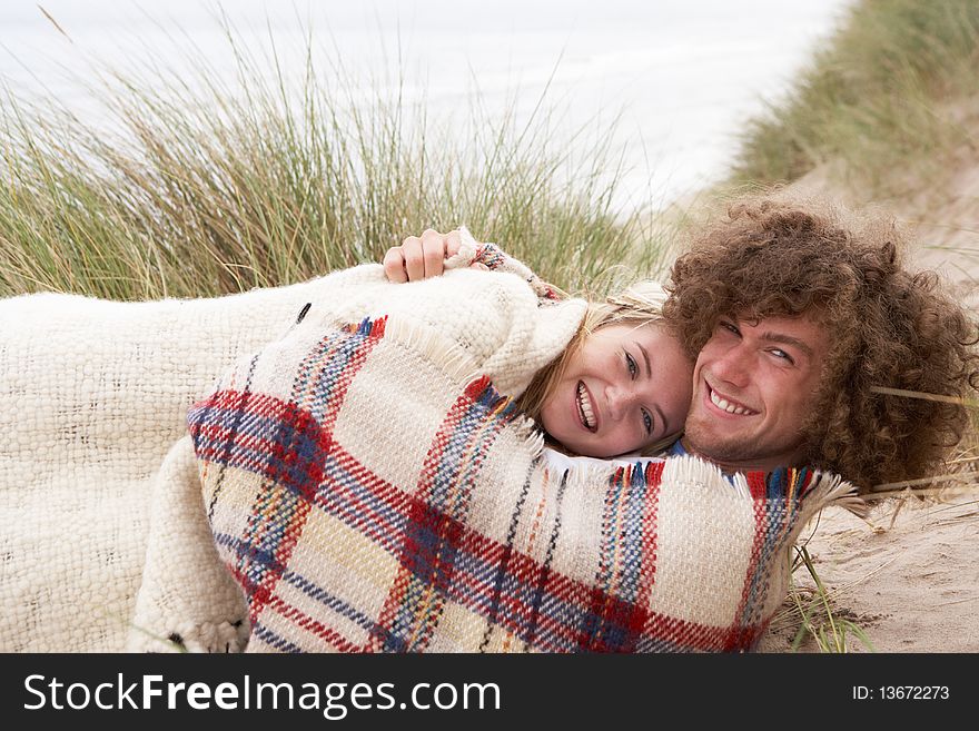 Teenage Couple Sitting In Sand Dunes Wrapped In Bl