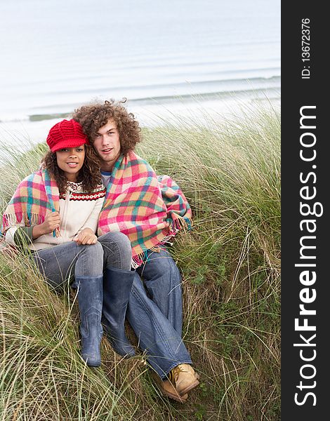 Young Couple Sitting In Sand Dunes Wrapped In Blanket