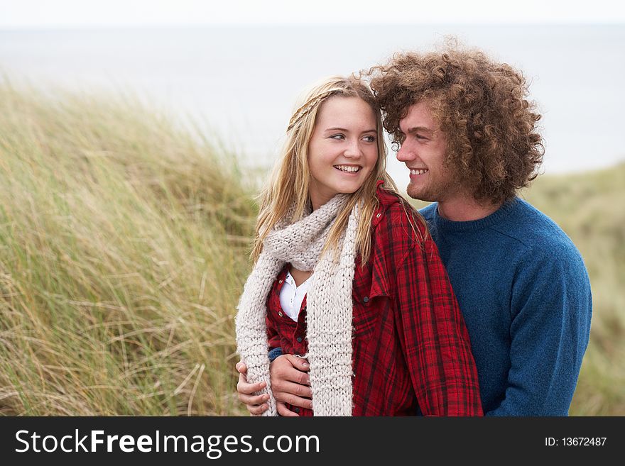 Teenage Couple Walking Through Sand Dunes Wearing Warm Clothing