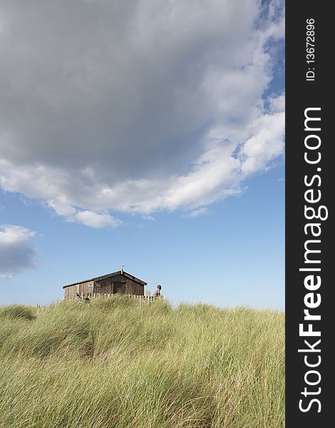 Distant View Of Young Couple Relaxing In Wooden Beach Hut Amongst Dunes