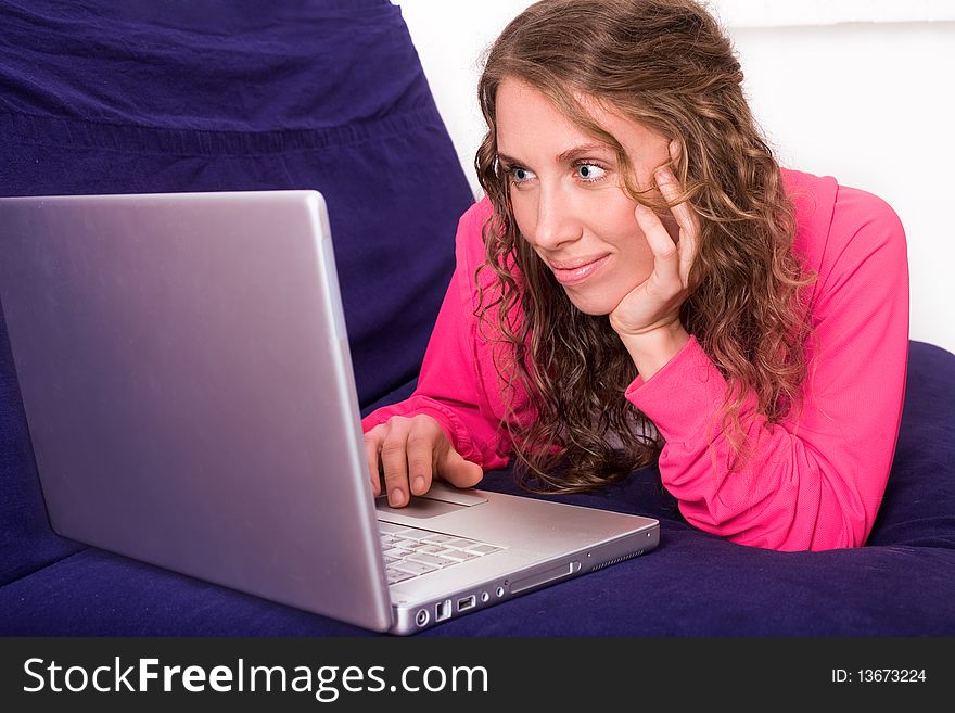 Young woman looks at laptop lying on the sofa. Young woman looks at laptop lying on the sofa