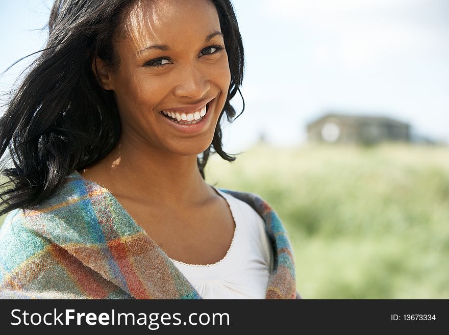 Smiing Young Woman Standing On Beach Wrapped In Blanket