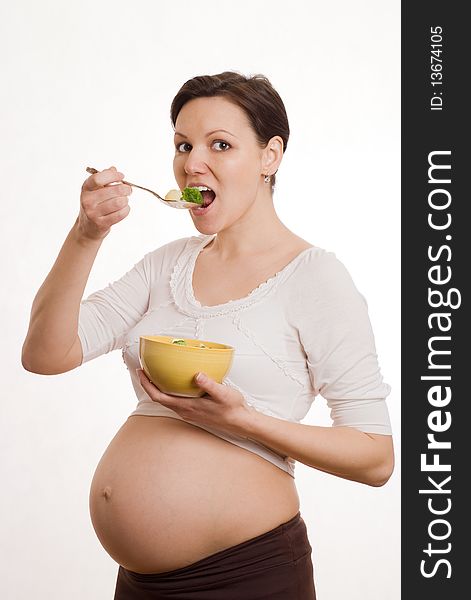 Beautiful young pregnant woman eats vegetables on white. Beautiful young pregnant woman eats vegetables on white