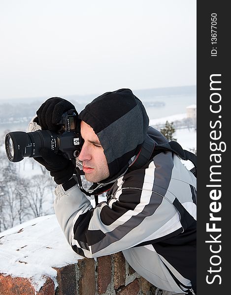 Young man, photographing in winter, focused and ready to shoot, leaning on a wall to stabilize his posture. Young man, photographing in winter, focused and ready to shoot, leaning on a wall to stabilize his posture