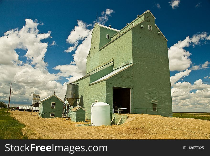 Old weathered light green painted wood grain elevator against sunny blue sky with white clouds. Names and logos removed. Old weathered light green painted wood grain elevator against sunny blue sky with white clouds. Names and logos removed.