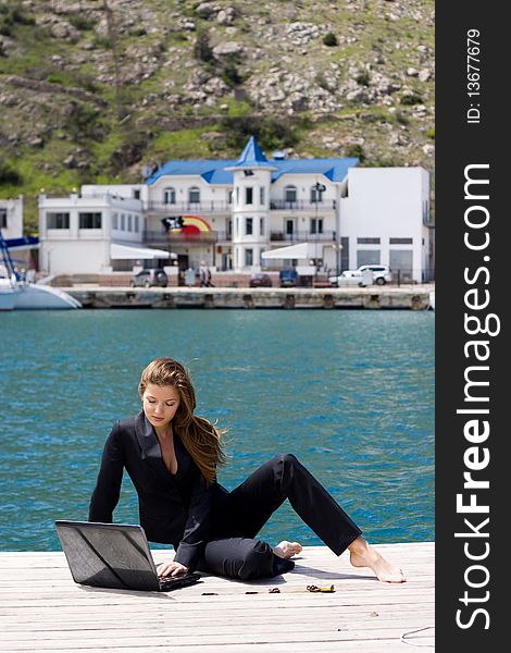 Woman in black business suit sitting with laptop near the sea. Woman in black business suit sitting with laptop near the sea