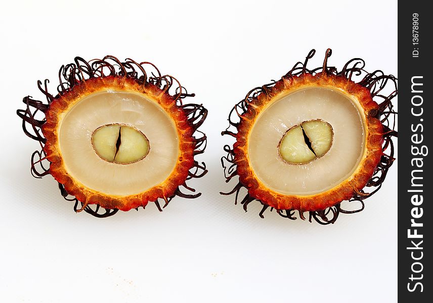 A close up of a rambutan fruit cut in two revealing the succulent white flesh protected by red hairy shell. A close up of a rambutan fruit cut in two revealing the succulent white flesh protected by red hairy shell.