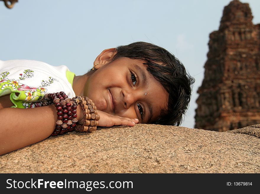 Girl child with ornamental hand bands enjoying rocky lap at Vijayavithala temple in Hampi, Karnataka, India, Asia