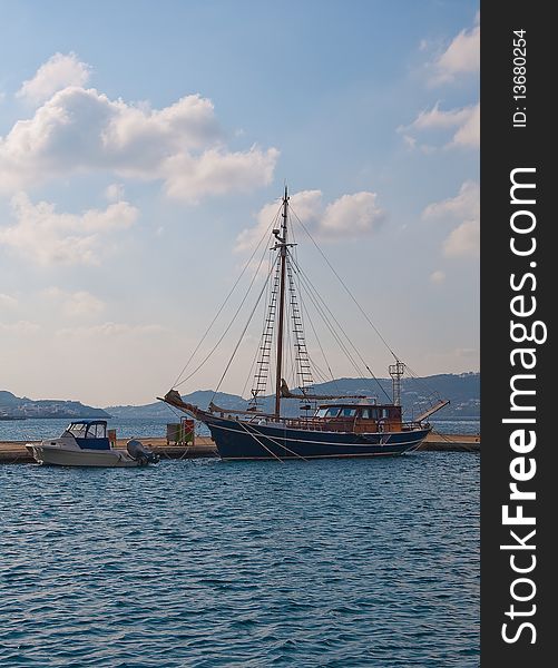 Pleasure yacht in the ancient style on parking in a bay on the island in the sun on the background of the sea and clouds. Pleasure yacht in the ancient style on parking in a bay on the island in the sun on the background of the sea and clouds