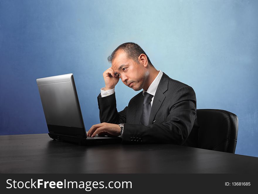 Japanese businessman sitting in front of a laptop and thinking